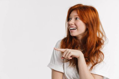 Ginger güzel, heyecanlı, gülümseyen ve işaret eden kız beyaz arka planda soyutlanmış.