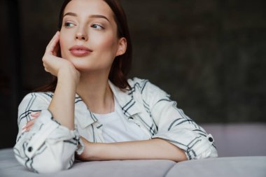 Güzel, memnun, hoş bir kadın, kanepede otururken yan bakıyor.