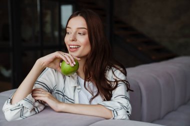 Güzel, mutlu, güzel bir kadın. Otururken gülümseyen ve elma yiyen.