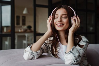 Güzel, mutlu, güzel bir kadın. Kulaklıkla müzik dinliyor. Kapalı koltukta oturuyor.