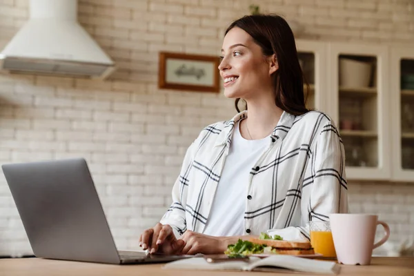 Hermosa Mujer Sonriente Que Trabaja Con Ordenador Portátil Mientras Desayuna —  Fotos de Stock