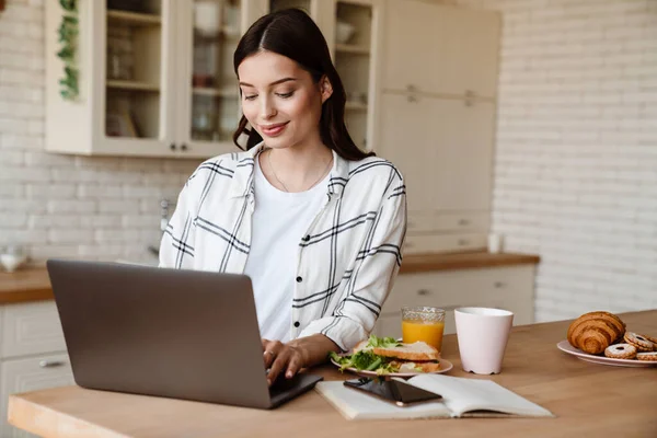 Gyönyörű Mosolygós Dolgozik Laptop Miközben Reggelizik Hangulatos Konyhában — Stock Fotó