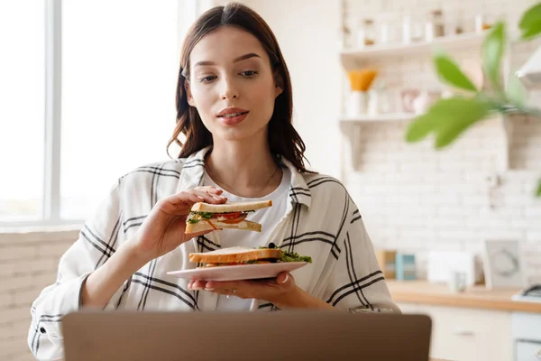 Hermosa Mujer Enfocada Trabajar Con Ordenador Portátil Mientras Come Sándwich — Foto de Stock