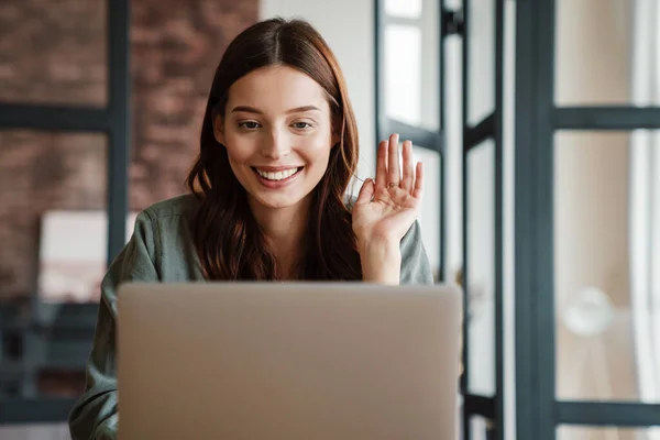 Mulher Sorridente Bonita Acenando Mão Trabalhando Com Laptop Enquanto Sentado — Fotografia de Stock