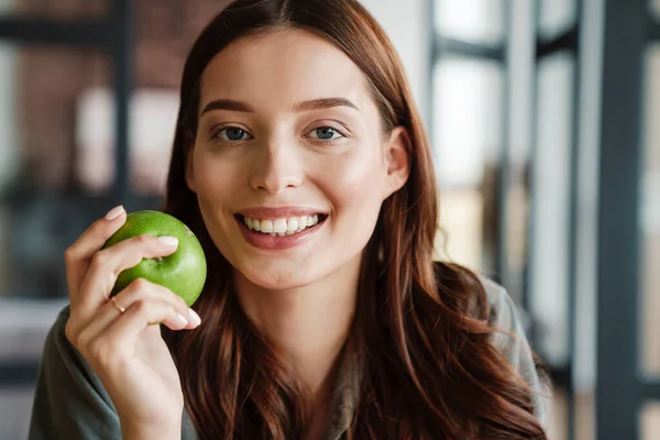 漂亮而快乐的女人在室内吃苹果时对着相机笑 — 图库照片