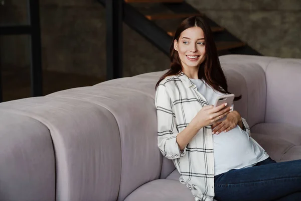 Feliz Mujer Embarazada Encantadora Usando Teléfono Móvil Mientras Está Sentado — Foto de Stock