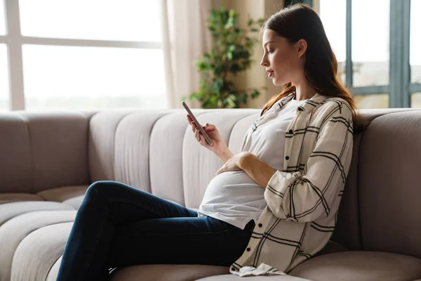 Enfocado Encantadora Mujer Embarazada Utilizando Teléfono Móvil Mientras Está Sentado — Foto de Stock