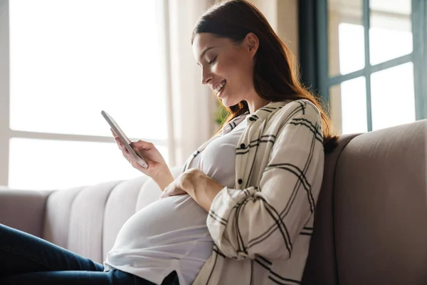 Feliz Mujer Embarazada Encantadora Usando Teléfono Móvil Mientras Está Sentado — Foto de Stock