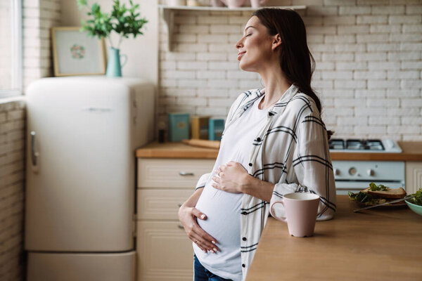 Pregnant happy nice woman smiling while having breakfast in home kitchen