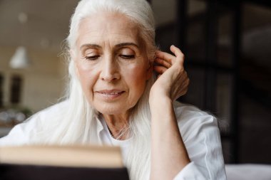 Oturma odasında oturmuş kitap okuyan kıdemli bir kadın.