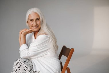 Gri arka planda izole edilmiş, gülümseyen ve kameraya bakan mutlu, beyaz saçlı bir kadın.