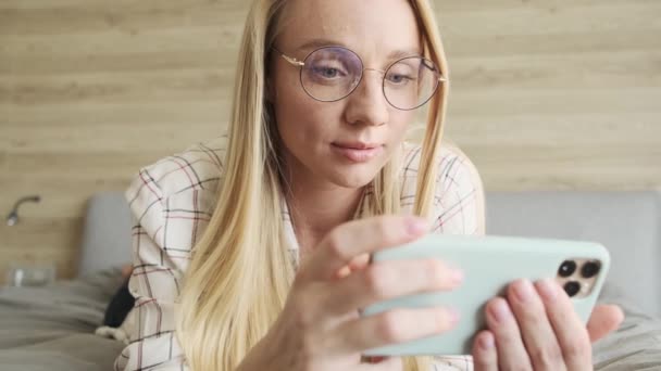 Potěšená Mladá Blondýnka Brýlemi Dívá Svůj Smartphone Zatímco Drží Horizontálně — Stock video