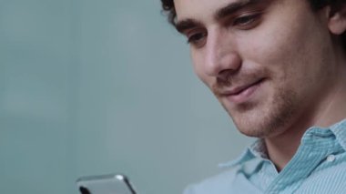 Gülümseyen bir iş adamının yakın çekim görüntüsü ofiste oturan akıllı telefonunu kullanıyor.