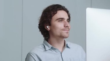 Kulaklık takan çekici bir işadamı ofiste internet bağlantısı ile konuşurken bilgisayarıyla çalışıyor.