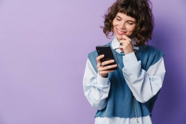 Akıllı telefon kullanan neşeli güzel bir kız ve mor arka planda izole edilmiş bir gülümseme.