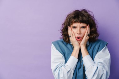 Şok olmuş beyaz bir kız, mor arka planda izole edilmiş bir şekilde kamerada şaşkınlığını dile getiriyor.
