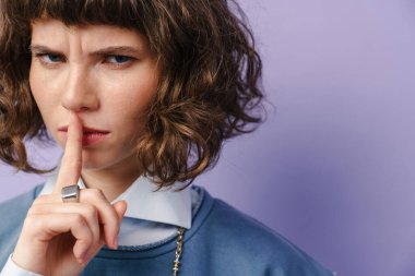 Mor arka planda izole edilmiş kameraya sessiz jest yapan güzel bir kız.