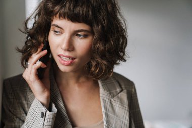 Kapalı alanda duvara yaslanırken akıllı telefondan konuşan güzel bir kız.