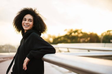 Şehir köprüsündeki korkuluklara gülümseyen ve yaslanan memnun sporcu kadın.
