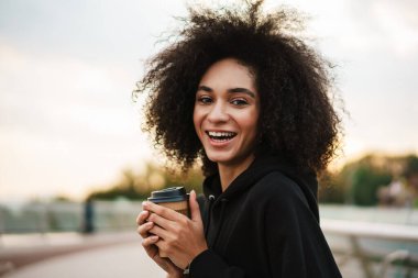 Neşeli, güzel sporcu kadın Köprü 'de gülümsüyor ve kahve içiyor.