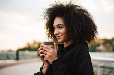 Neşeli, güzel sporcu kadın Köprü 'de gülümsüyor ve kahve içiyor.