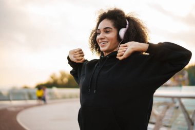 Şehir köprüsünde egzersiz yaparken kulaklıklı mutlu bir sporcu kadın.