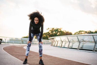 Gülümseyen Afrikalı genç sporcu kadın dışarıda koştuktan sonra dinleniyor.