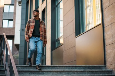 Kendine güvenen, şık, Afro-Amerikan bir adam sokakta yürüyor.