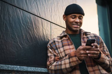 Çekici, mutlu, genç bir Afrikalı adam cep telefonuyla sokakta yürüyor.