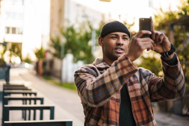 Çekici genç Afrikalı adam sokakta yürürken fotoğraf çekiyor.