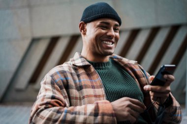 Çekici gülümseyen genç Afrikalı bir adam cep telefonuyla sokakta yürüyor.