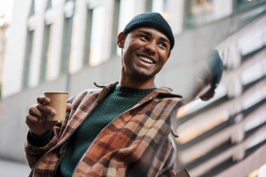 Yakışıklı Afrikalı bir adam sokakta yürürken kahve içiyor.