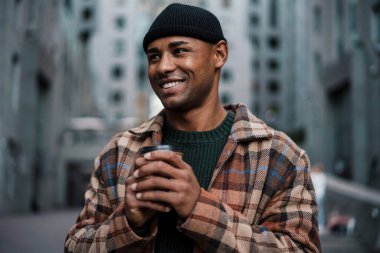 Yakışıklı Afrikalı bir adam sokakta yürürken kahve içiyor.
