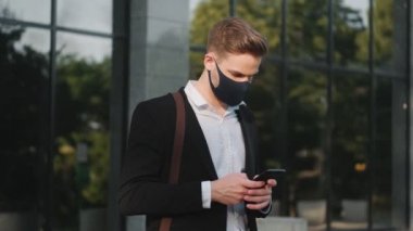 Koruyucu maske takan yakışıklı bir işadamı dışarıda duran telefonu kullanıyor.