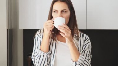 Güzel genç bir kadın evde mutfakta otururken bir fincan kahve içiyor.