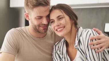 Gülümseyen genç bir çift kadın ve erkek evdeki mutfakta birlikte oturuyorlar.