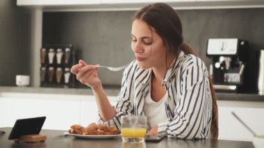 Çekici genç bir kadın evdeki mutfakta kahvaltı yapıyor.