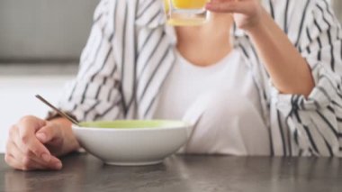 Genç bir kadının kırpılmış görüntüsü, evdeki mutfakta kahvaltıda portakal suyu içiyor.