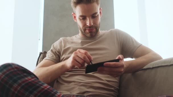 Thinking Concentrated Young Man Using His Smartphone Stylus Sitting Sofa — Stock Video