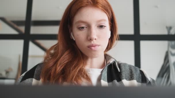 Focused Redhead Woman Earbuds Using Her Laptop Computer Sitting Apartments — Stock Video