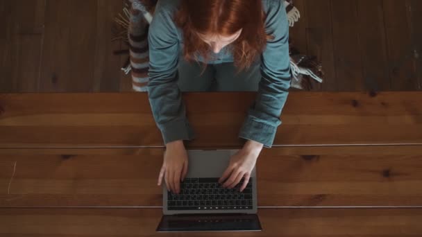 一位红头发的年轻女士坐在公寓桌子旁的笔记本电脑键盘上打字 这是一张她的头像 — 图库视频影像