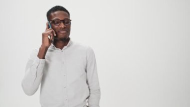 Gözlüklü, gülümseyen Afrikalı bir Amerikalı akıllı telefonuyla konuşuyor. Stüdyoda beyaz arka planda tek başına duruyor.