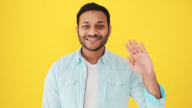 Dost canlısı bir Hintli selam veriyor. Stüdyoda sarı arka planda duruyor.
