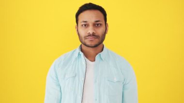 Kendine güvenen bir Hintli, stüdyoda sarı arka planda durarak dur hareketi yapıyor.