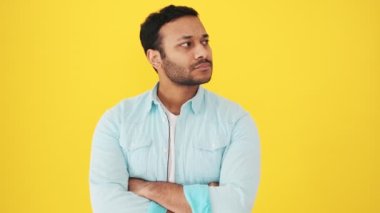 Sakin odaklı Hintli bir adam stüdyoda sarı arka planda duran bir şey düşünüyor.