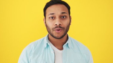 Mutlu ve şaşırmış Hintli bir adamın yakın çekim görüntüsü stüdyoda sarı arka planda tek başına duran kameraya bakıyor.
