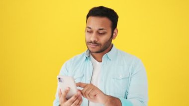 Memnun Hintli bir adam, kendi fotoğrafını çekerken akıllı telefonunu kullanıyor ve onu stüdyonun sarı arka planında izole bir şekilde duruyor.