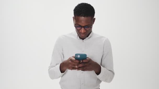 Zadowolony Afrykanin Okularach Używa Swojego Smartfona Stojącego Białym Tle Studiu — Wideo stockowe