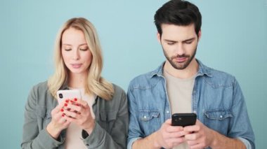 Gülümseyen erkek ve kadın akıllı telefonlarını stüdyodaki mavi arka planda tek başlarına duruyorlar.