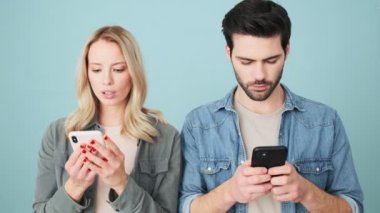 Şok olmuş bir kadın, erkek arkadaşının telefonuna bakıyor. Stüdyonun mavi arka planında tek başına duruyor.